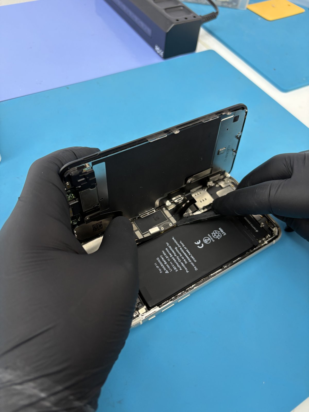 Nahaufnahme eines Smartphones mit gesprungenem Display auf einem Tisch, daneben Werkzeug aus einer Handywerkstatt in Regensburg.